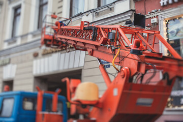 Aerial work platform vehicle during facade decoration, orange telescopic elevator on construction site, rental AWP working in the city streets, engineer working on heights