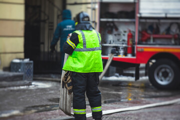 Fototapeta premium Group of fire men in uniform during fire fighting operation in the city streets, firefighters with the fire engine truck fighting vehicle in the background, emergency and rescue