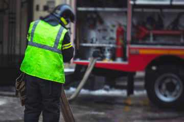 Group of fire men in uniform during fire fighting operation in the city streets, firefighters with the fire engine truck fighting vehicle in the background, emergency and rescue