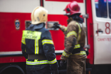 Group of fire men in uniform during fire fighting operation in the city streets, firefighters with the fire engine truck fighting vehicle in the background, emergency and rescue