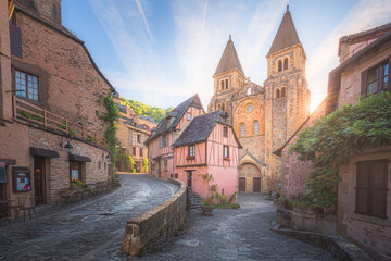 The quaint and charming town centre of the  medieval French village Conques, Aveyron and Abbey Church of Sainte-Foy at sunset or sunrise in Occitanie, France. - obrazy, fototapety, plakaty