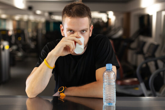 Man Drinking Water While Resting In A Generic Out Of Focus Fitness Club.