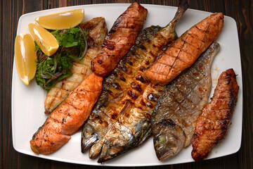 Grilled fish on a white plate with herbs and lemon, dorado, mackerel, salmon steak, salmon fillet, on a wooden board