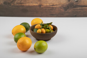 Bowl of fresh kumquats, limes and lemons on white background