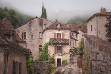 The quaint and charming French medieval hilltop village of Saint-Cirq-Lapopie on a foggy, misty morning in the Lot Valley, France.