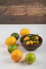 Bowl of fresh kumquats, limes and lemons on white background