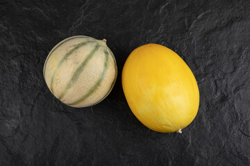 Fresh ripe yellow and green melons on black surface