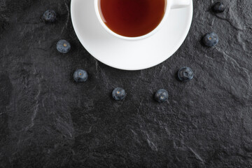 Cup of tea and delicious fresh blueberries on black surface
