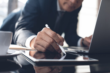 Businessman using touchscreen pen on digital tablet and working on  laptop computer at modern office