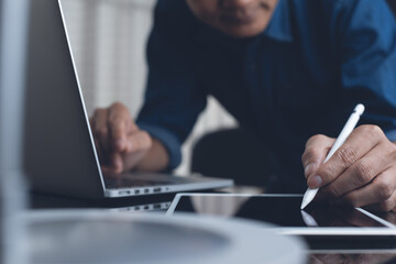 Man using touchscreen pen on digital table and working on laptop computer on office table