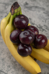 Fresh healthy plums with banana cluster on stone background