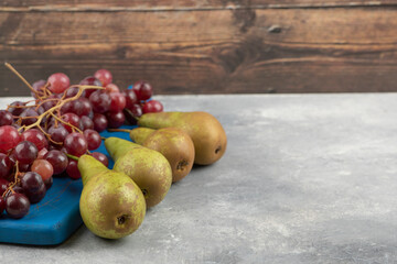 Red grapes on blue cutting board with ripe pears on marble surface