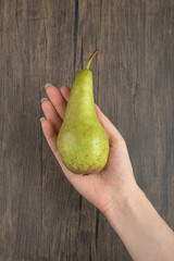 Female hand holding single ripe pear on wooden surface
