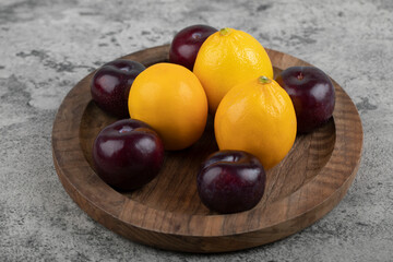 A wooden plate of purple plums and fresh lemons on stone background
