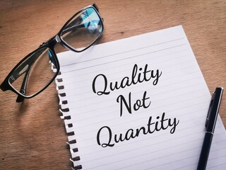 Business concept. Selective focus a piece of paper  written phrase QUALITY NOT QUANTITY with a pen and eye glasses.