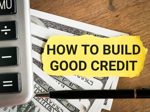 Phrase HOW TO BUILD GOOD CREDIT written on yellow paper strip with calculator, pen and fake money. Business and finance concept. 