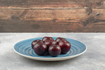 Blue plate of fresh purple plums on marble surface