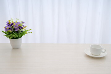 A white coffee cup and a pot of purple artificial bouquet on the table, white gauze curtain background with copy space, minimalist desk