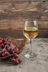 Wicker basket of red grapes with glass of white wine on marble table