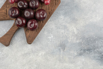 Wooden board of fresh red plums and grapes on marble surface