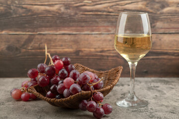 Wicker basket of red grapes with glass of wine on marble table