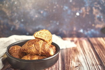 Bowl negro lleno de croasants fresco sobre tabla de madera