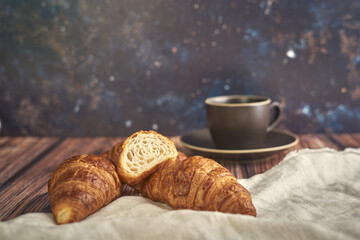 Three croissants on canvas and wooden background, with coffee cup for breakfast.