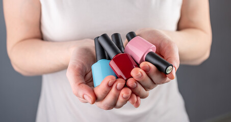 Woman is holding a variety of colorful bottles of nail polish in her hands. Closeup. Concept of choosing a color for manicure