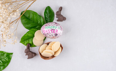 Shiny Easter egg, rabbit shaped chocolate and fresh spring leaves on a white background. Top view, copy space