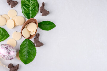 Fototapeta na wymiar Shiny Easter egg, bunny shaped chocolate and fresh spring leaves on a white background. Top view, copy space