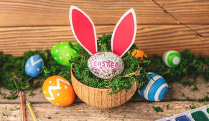 Obraz na płótnie Canvas Bright colorful Easter eggs and rabbit ears on a wooden background covered with green moss