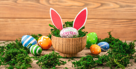 Bright colorful Easter eggs and rabbit ears on a wooden background covered with green moss