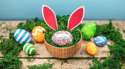 Obraz na płótnie Canvas Bright colorful Easter eggs and rabbit ears on a blue and wooden background with green moss