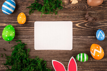 Bright Easter card with colorful eggs, paper rabbit ears and green moss on a wooden background. Copy space and top view