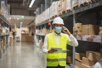 Soft focus asian engineer or technician wearing mask,safety hard hat,uses digital tablet check merchandise stock,security cargo management,in warehouse,industry business  logistic and export concept