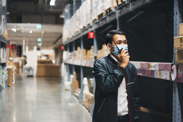 Soft focus Asian engineer or technician wearing mask,safety hard hat,uses radio communication check merchandise stock,security cargo management,warehouse,industry business logistic and export concept