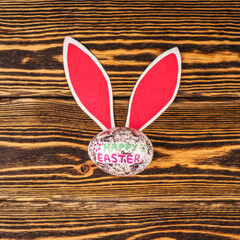 Shiny Easter egg with paper rabbit ears on wooden background. Top view