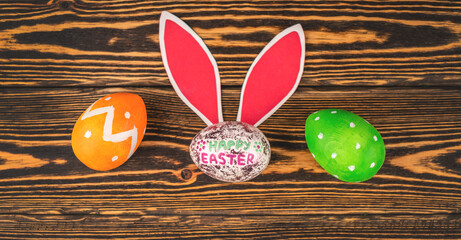 Bright Easter card with colorful eggs, paper rabbit ears on a wooden background. Top view