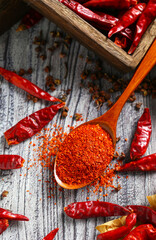 Chili powder in wooden spoon and dry pepper on grey wooden table