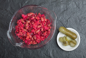 Glass bowl of pickled cabbage with red beans and cucumbers on black background