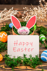 Cute bright Easter card with colorful eggs, paper rabbit ears and green moss on a wooden background