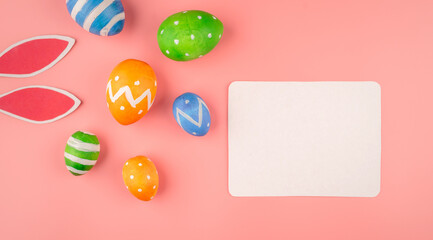 Bright Easter card with colorful eggs, paper rabbit ears on a pink background. Copy space and top view