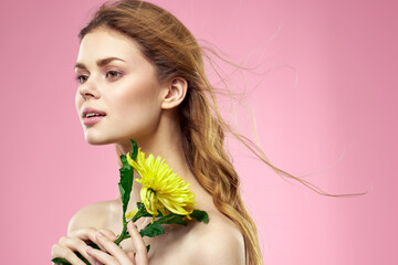 Fototapeta premium Beautiful girl with a yellow flower on a pink background nude shoulders makeup