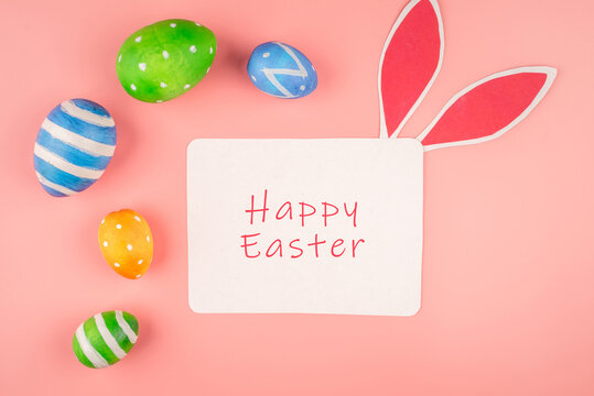 Bright Easter card with colorful eggs, paper rabbit ears on a pink background. Top view