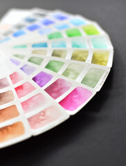 Watercolor color palette on white paper, fanned out. On a black background.