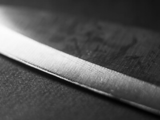 Close-up photo of a kitchen knife blade at an angle on a black background.