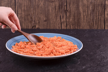 Woman hand taking raw pasta in hearts shape with wooden spoon on black table