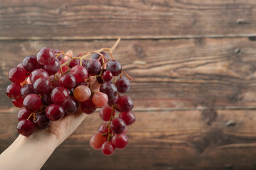 Woman hand holding cluster of red grapes on wooden background
