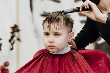 Close-up of woman hands grooming kid boy hair in barber shop.