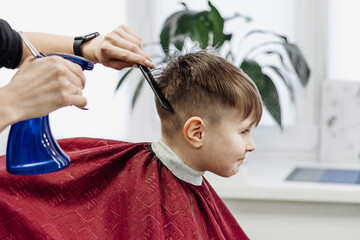 Barber's hands spray the little boy's hair with a spray gun.